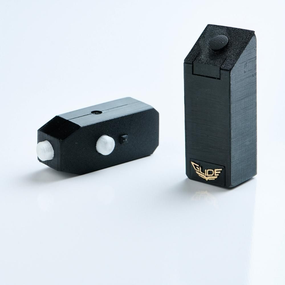 Two black rectangular electronic devices with white buttons are shown on a white background. One is standing upright with a gold GLIDE logo, while the other is lying flat.