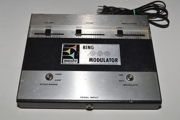 A vintage Maestro Ring Modulator effects pedal with three sliders labeled Volume, Pitch, and Modulation, a logo, a toggle switch, and a black power cord. The unit has a metallic and black design.