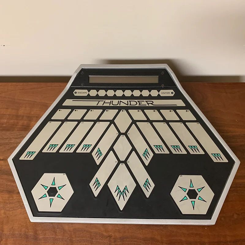 A hexagonal electronic drum pad labeled THUNDER with multiple touch-sensitive pads and geometric star patterns, resting on a wooden surface against a plain background.