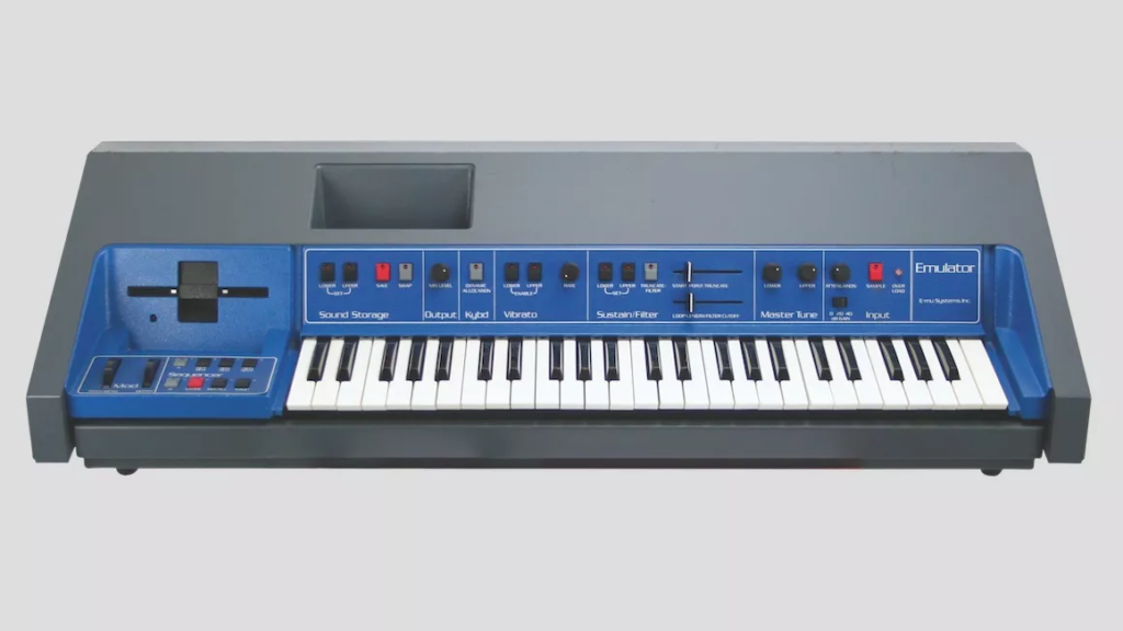 A vintage blue and black keyboard synthesizer with various control buttons, knobs, and sliders above the keys, labeled “Emulator” on the right side against a plain gray background.