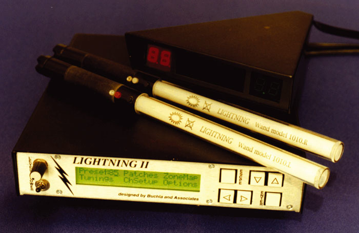 A close-up of an electronic device labeled LIGHTNING II with buttons and a display, two wand-like instruments, and a small black digital display box with red LED numbers, all placed on a blue surface.