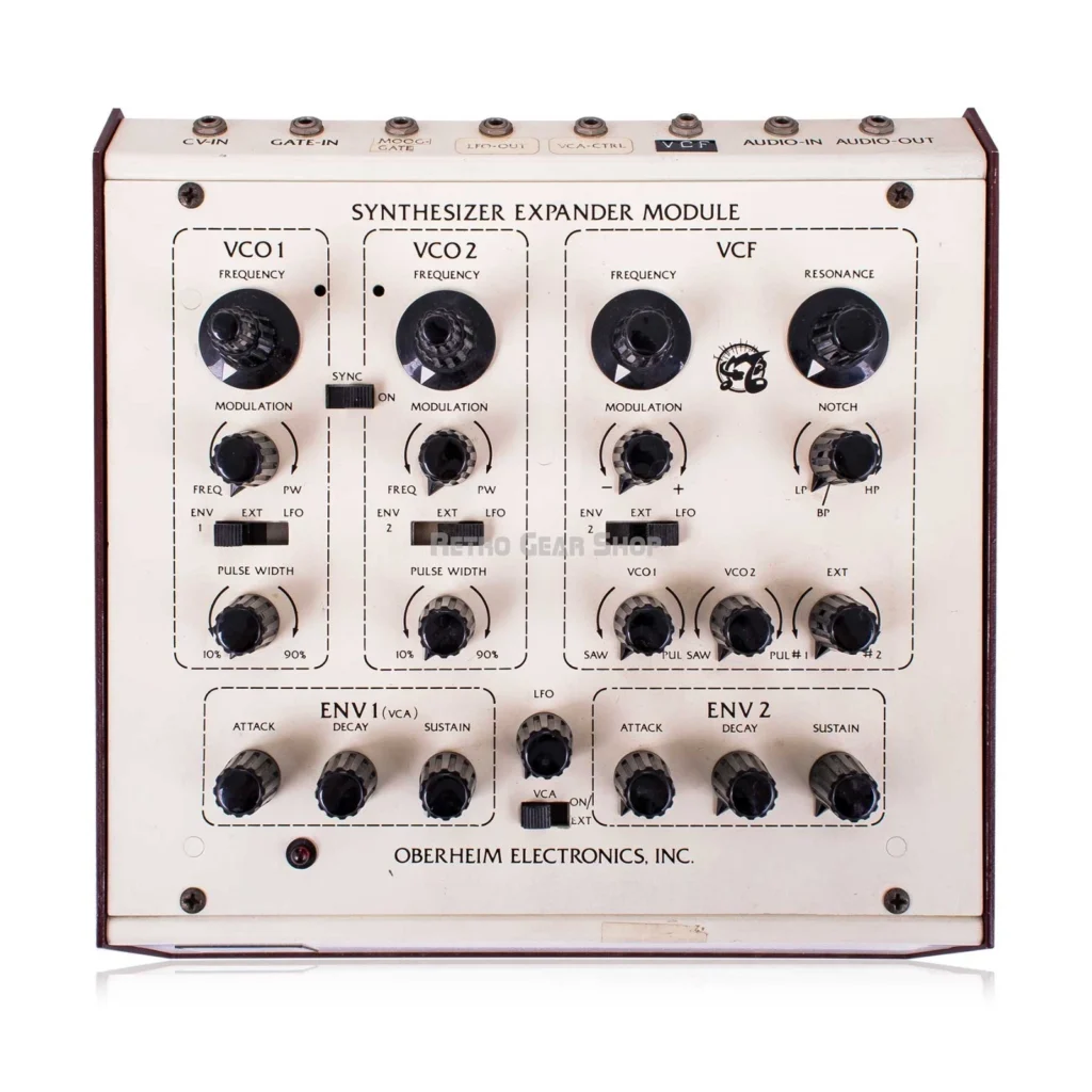 Front view of a vintage Oberheim Synthesizer Expander Module with various black knobs, switches, and labeled sections for VCO1, VCO2, VCF, ENV1, and ENV2 on a white panel.
