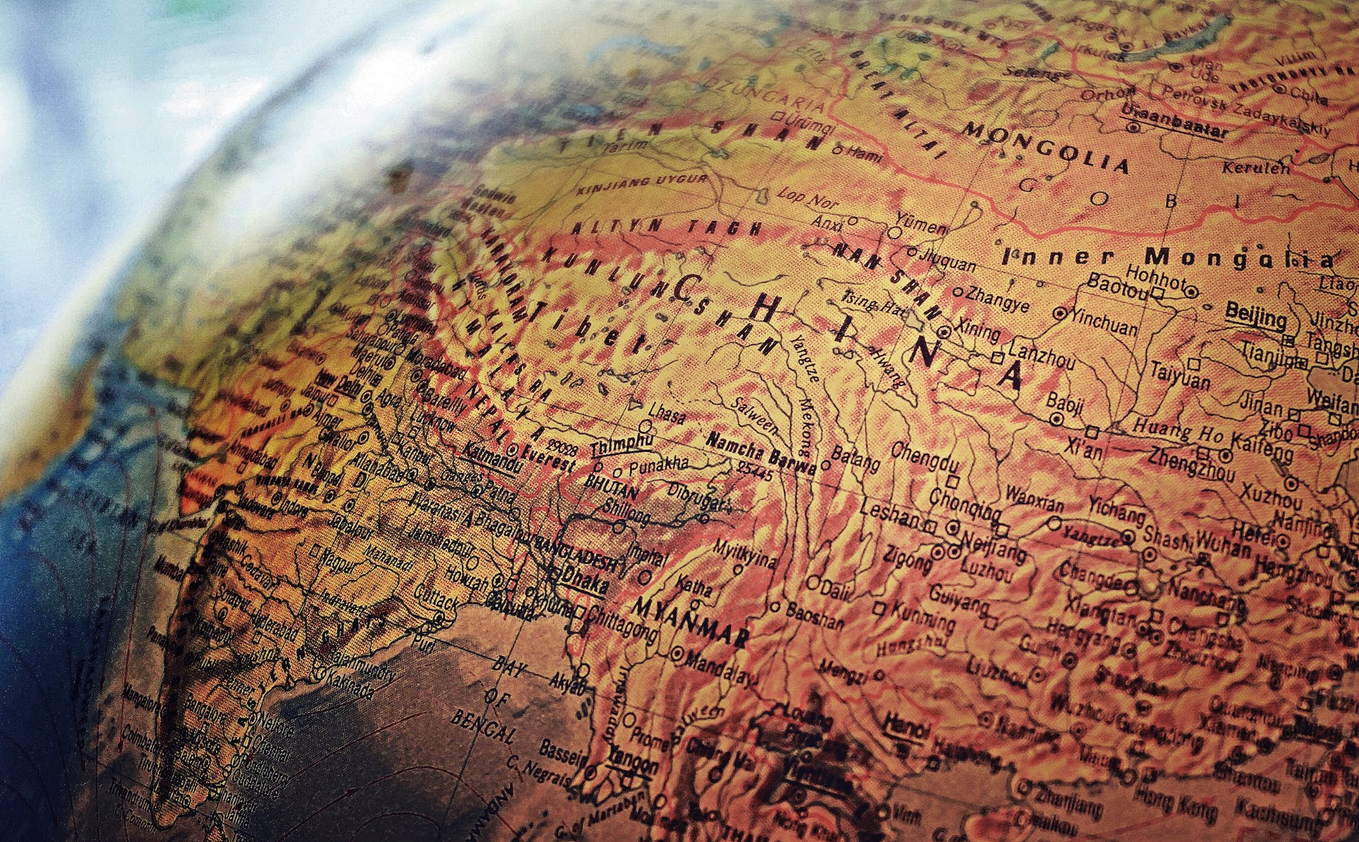 A close-up of a globe showing detailed topography and country names in Asia, including China, Mongolia, India, and surrounding regions, with mountain ranges and borders clearly visible.