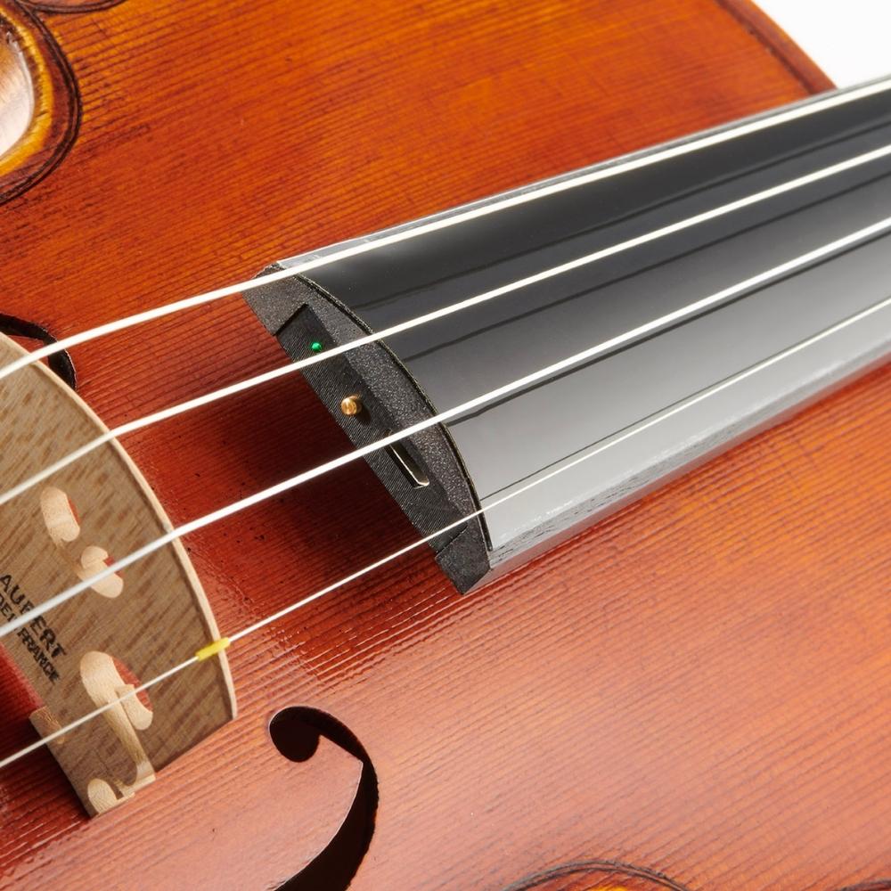 Close-up of a violin showing its wooden body, bridge, four strings, and a black electronic fingerboard attachment with a small green light indicator.