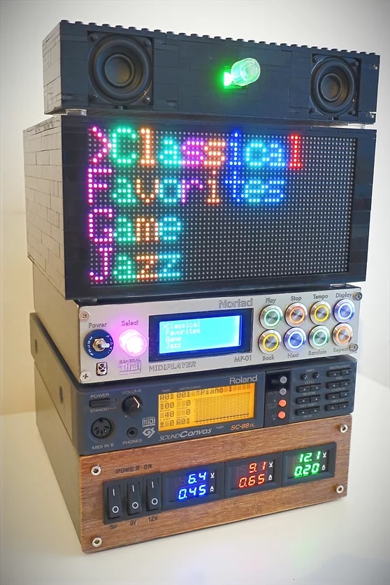 A stack of colorful, retro-style electronic music equipment with LED displays, buttons, knobs, meters, and speakers; the top display reads “Classical, Favorites, Jazz” in bright colors.