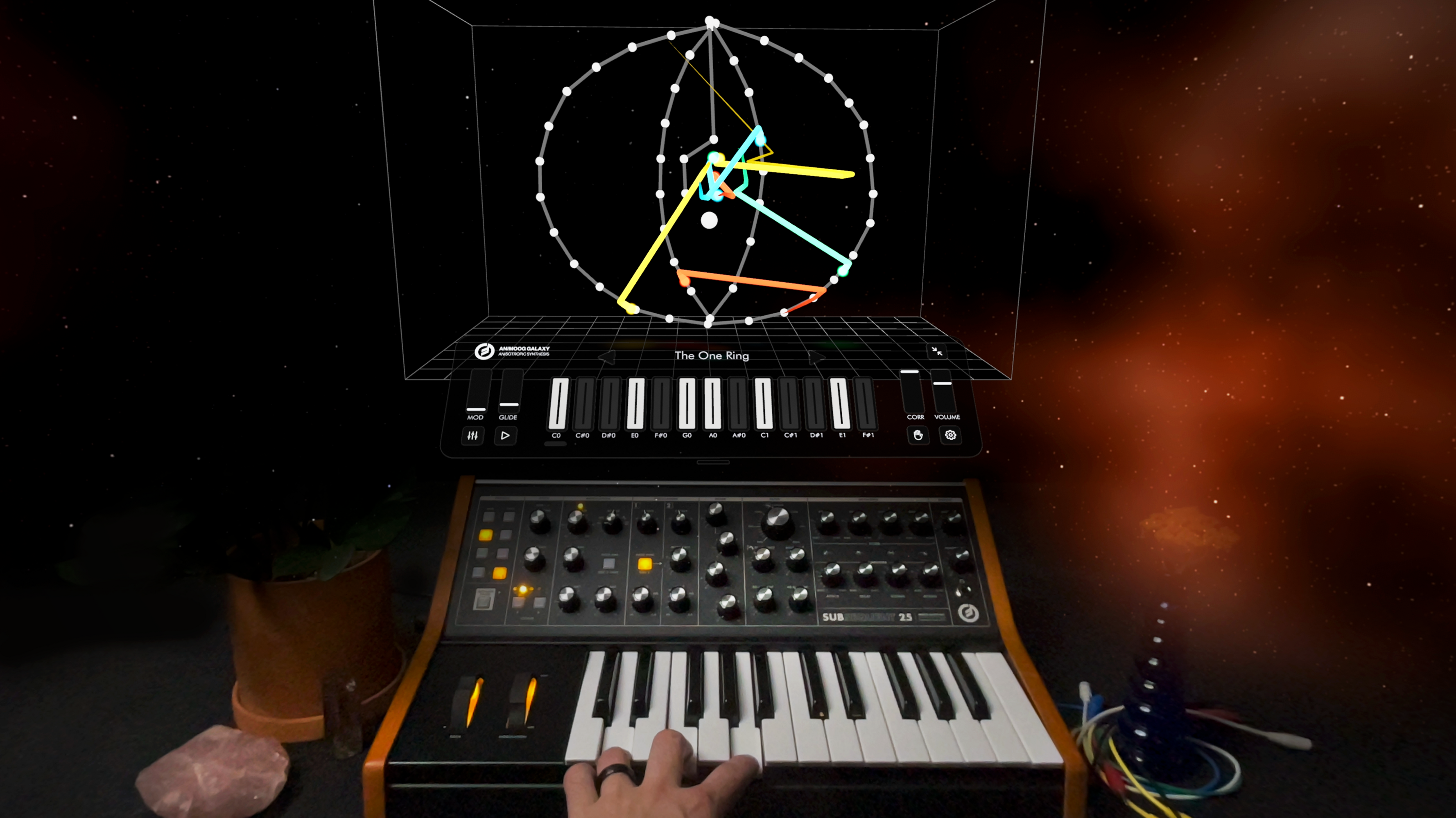 A hand plays a synthesizer keyboard below a digital screen displaying geometric shapes and lines forming a circular diagram, suggesting sound visualization. The background is dark with hints of orange and space-like elements.