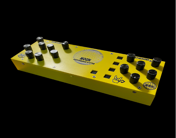 A bright yellow electronic synthesizer with multiple black knobs, silver dials, and square buttons, seen on a black background. The device is labeled “MDM” and has various symbols and text printed on its surface.