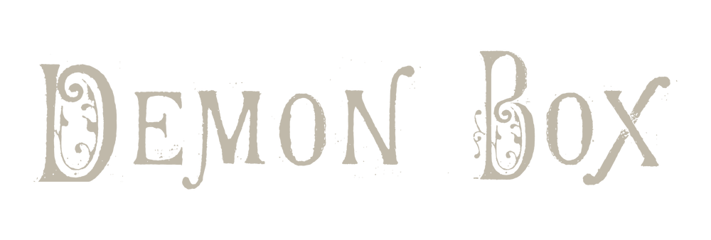 The words Demon Box are written in a decorative, vintage-style font with ornamental swirls on some letters. The text is beige on a transparent background.