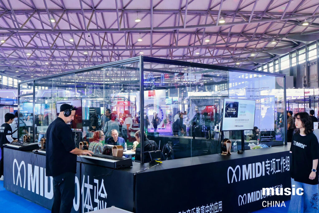 A booth at a busy expo showcases MIDI music technology. People interact with equipment inside a glass enclosure, while others observe. Bright lights and banners fill the spacious, industrial hall. “music CHINA” is visible in the corner.