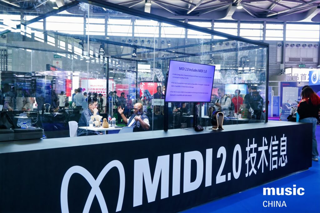 A booth at an expo displays MIDI 2.0 技术信息 (Technology Information) with people seated inside a glass enclosure. A monitor presents details, and music CHINA is visible on the counter.