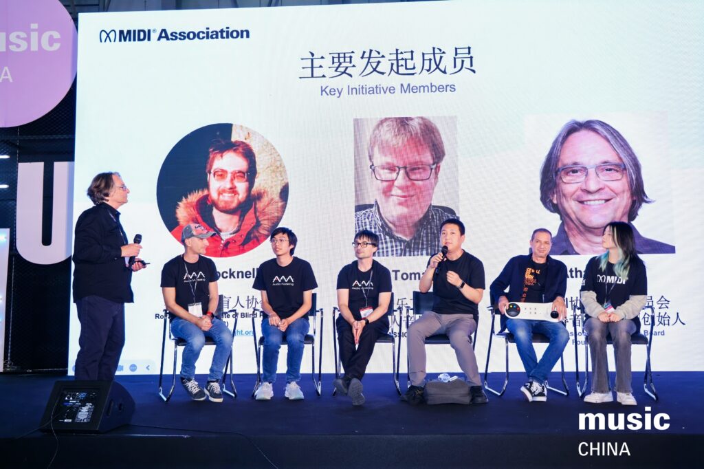 A group of six people sit and stand on a stage under a large screen displaying photos and names of key initiative members at a MIDI Association event, with music CHINA text visible in the lower right corner.