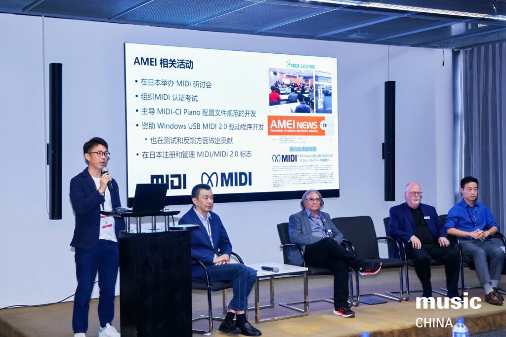 Four men sit on a panel, with one standing and speaking into a microphone. A large screen behind them displays information about AMEI MIDI activities in Chinese. The event is labeled “music CHINA.”.