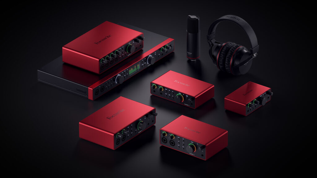 A collection of red Focusrite audio interfaces, a pair of black headphones, and a black microphone are arranged on a dark background. The devices feature various knobs, buttons, and input ports, showcasing a professional audio setup.