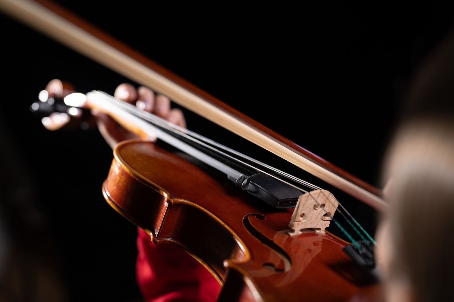 Close-up of a person playing a violin, focusing on the bow and strings, with the violinist’s hand pressing the strings on the fingerboard. The background is dark, highlighting the instrument.