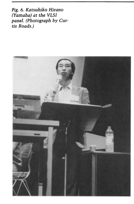 A man stands at a lectern speaking into a microphone during a panel event. There is a water bottle and some papers on a nearby table. A caption above the image identifies him as Katsuhiko Hirano at the VLSI panel.