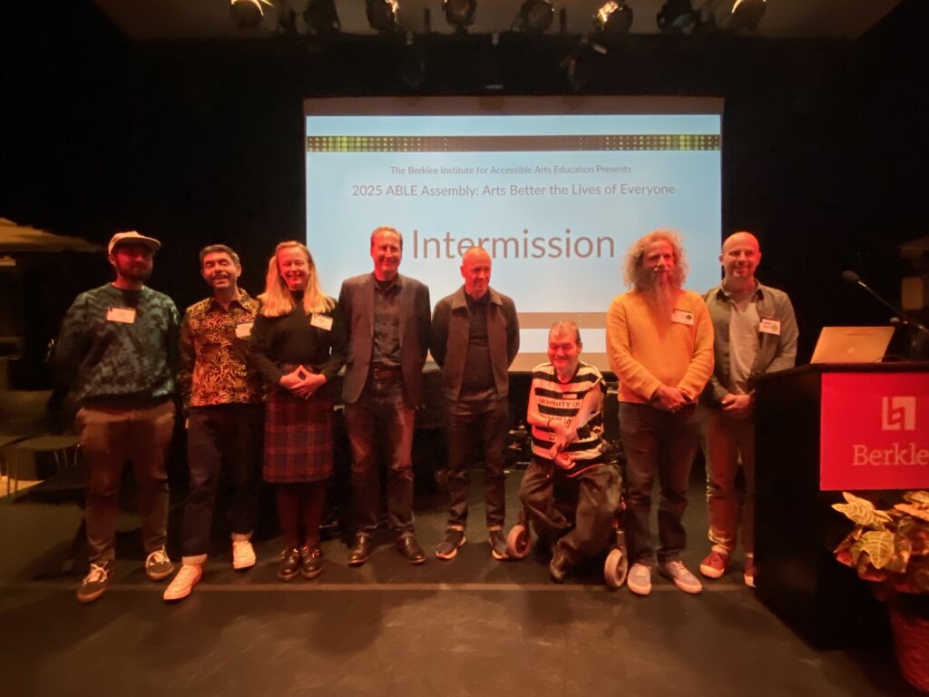 Eight people stand side by side on stage, smiling at the camera, in front of a large screen displaying the text 2025 ABLE Assembly: Arts Better the Lives of Everyone – Intermission at Berklee.