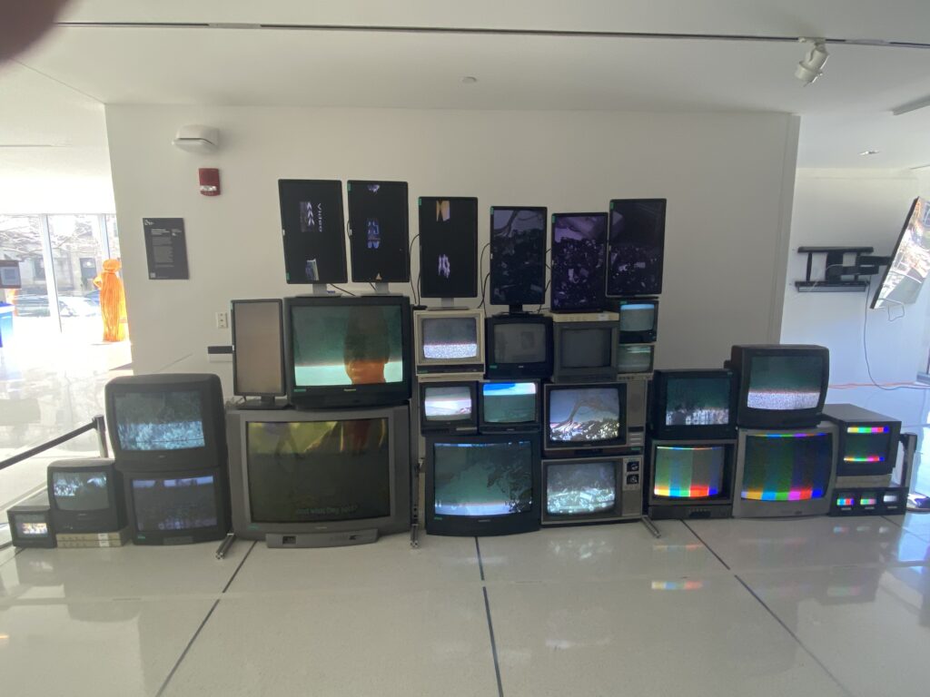 Picture from the first floor of the MIT Media Lab of a wall of old TVs in different condition and showing content on every screen. 