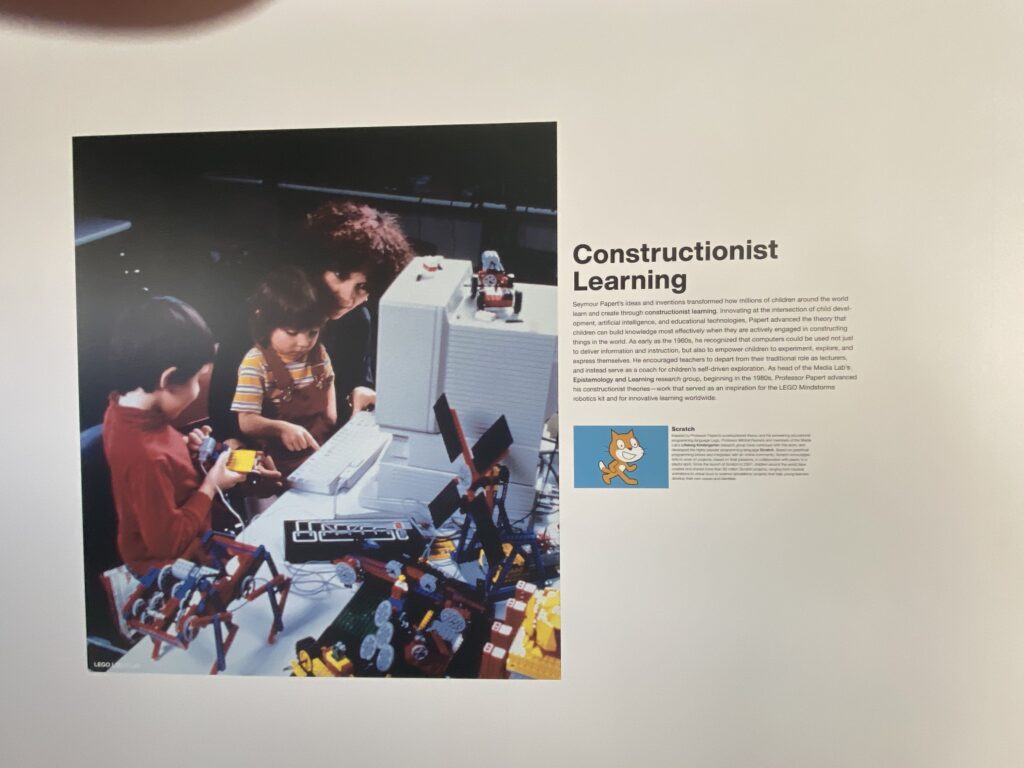 Three children gather around a computer on a desk, interacting with LEGO robotics and electronic components. The heading Constructionist Learning and a paragraph of text are displayed to the right of the photo.