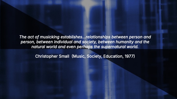 White text on a blue and black background reads: “The act of musicking establishes…relationships between person and person, between individual and society, between humanity and the natural world and even perhaps the supernatural world. Christopher Small (Music, Society, Education, 1977).”.