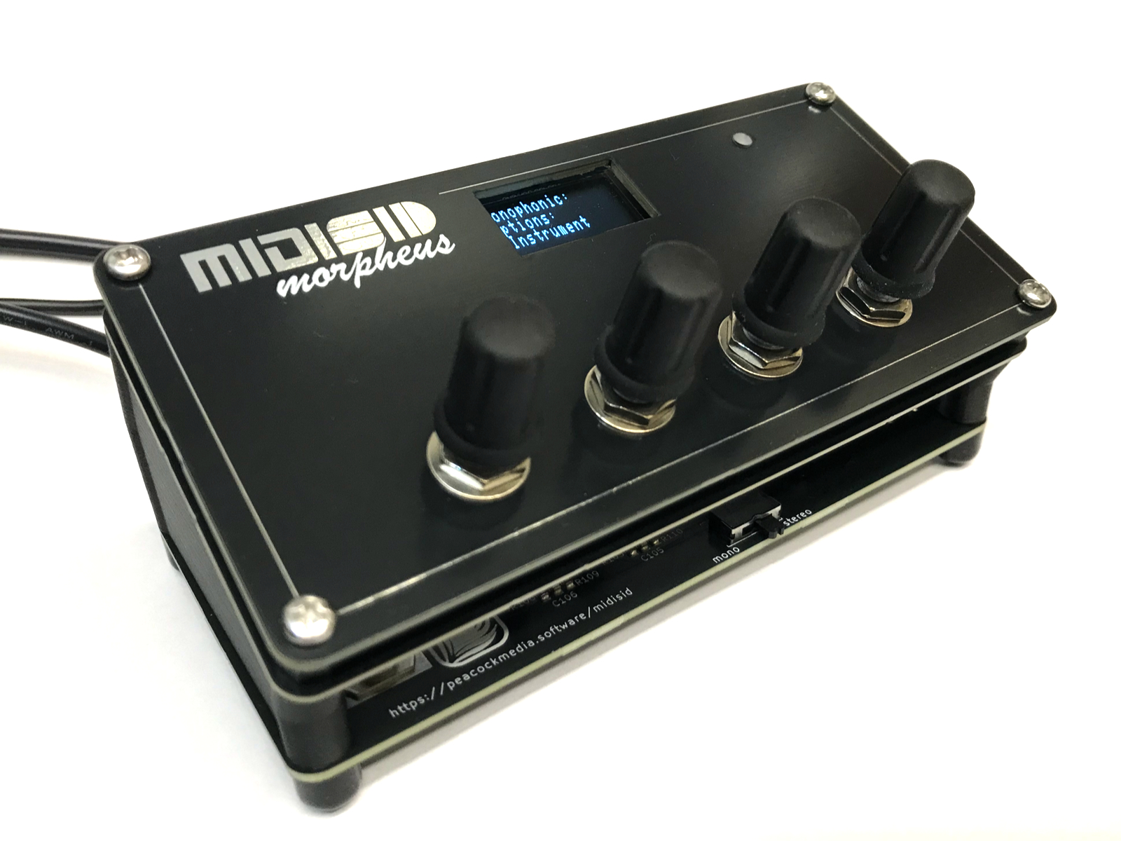 A black MIDI controller labeled MIDI Morpheus features four black control knobs and a small display screen showing settings. The device sits on a white background with visible cables connected.