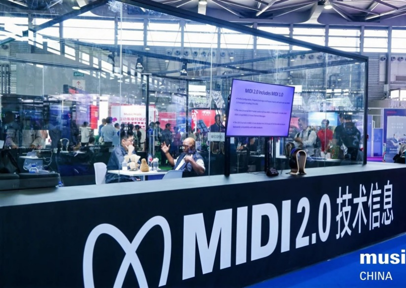 A glass booth at a trade show displays MIDI 2.0 技术信息 and MIDI 2.0 on the front, with people inside working on computers and a screen showing MIDI 2.0 information. Banners and attendees are visible in the background.