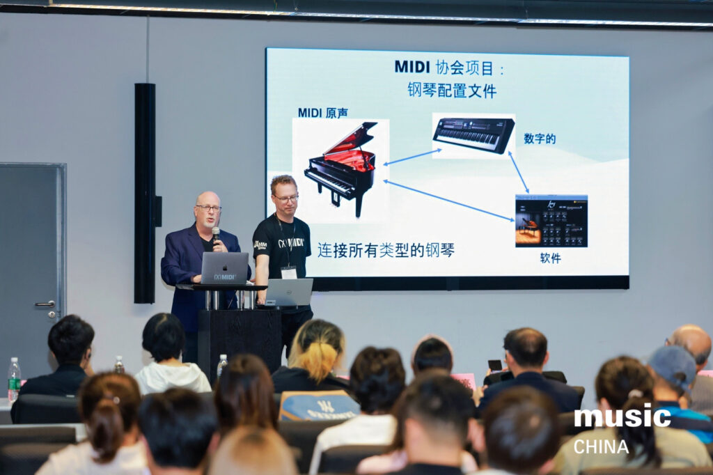 Two presenters stand at a podium, speaking to an audience. Behind them is a large screen displaying information about MIDI and keyboard configuration in Chinese, with images of a piano, keyboard, and software. music CHINA logo is visible.