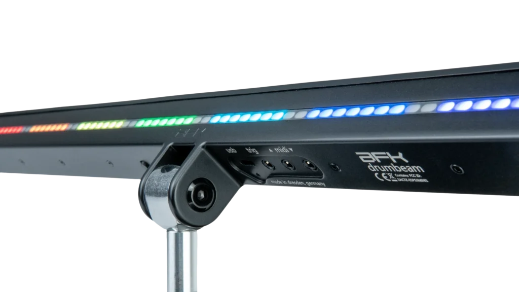 A close-up of an AFX drumbeam LED light bar showing a line of multicolored lights and control ports on its side, mounted on a metal stand against a black background.