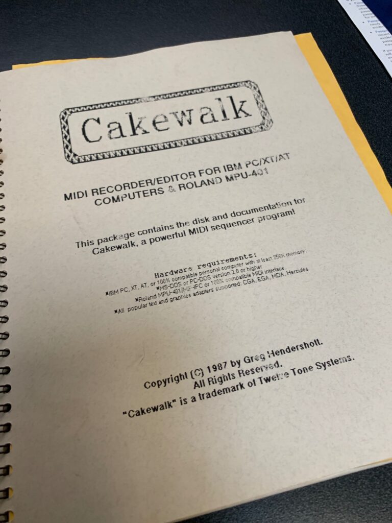 A spiral-bound manual titled “Cakewalk: MIDI Recorder/Editor for IBM PC/XT/AT Computers & Roland MPU-401” is shown lying on a dark surface, with visible copyright information and hardware requirements.