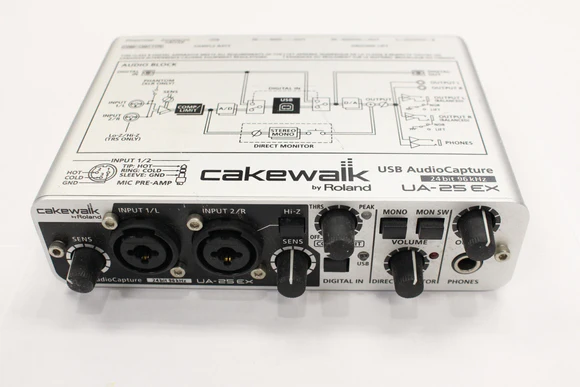 A Cakewalk UA-25EX USB AudioCapture by Roland audio interface with various input/output jacks, control knobs, and buttons on a white surface. Technical diagrams are printed on the device’s top panel.