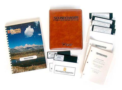 An assortment of vintage computer software items, including a spiral-bound manual with a nature cover, a brown binder labeled Soundchaser Computer Music System, floppy disks, and several instruction booklets.