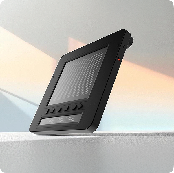 A sleek black electronic device with a raised dotted screen and tactile buttons is displayed on a light surface, with soft pastel shadows in the background.