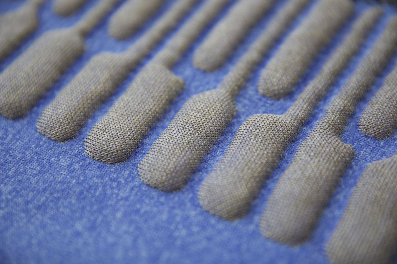 Close-up of a blue fabric with raised, elongated oval shapes in a row, creating a textured, three-dimensional pattern.