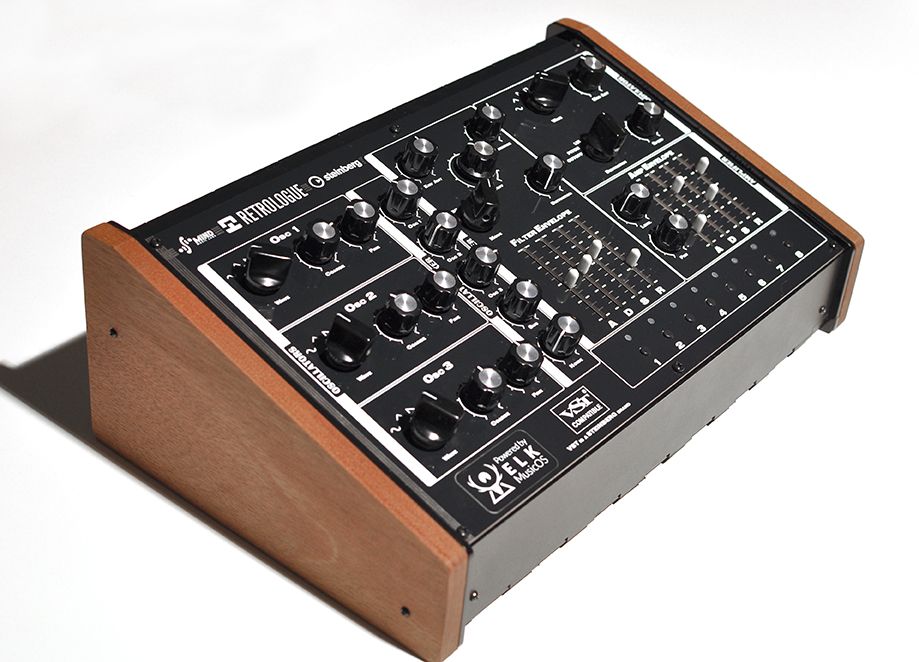 A black analog synthesizer with multiple knobs and switches, angled slightly to the right, featuring wooden side panels and various labeled controls on its surface.